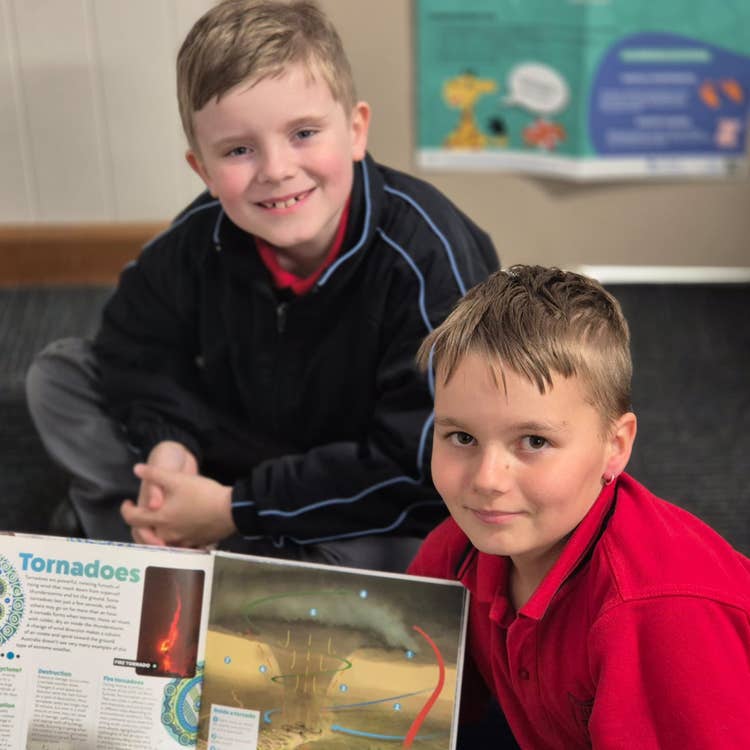 Two students smiling at camera showing an open book