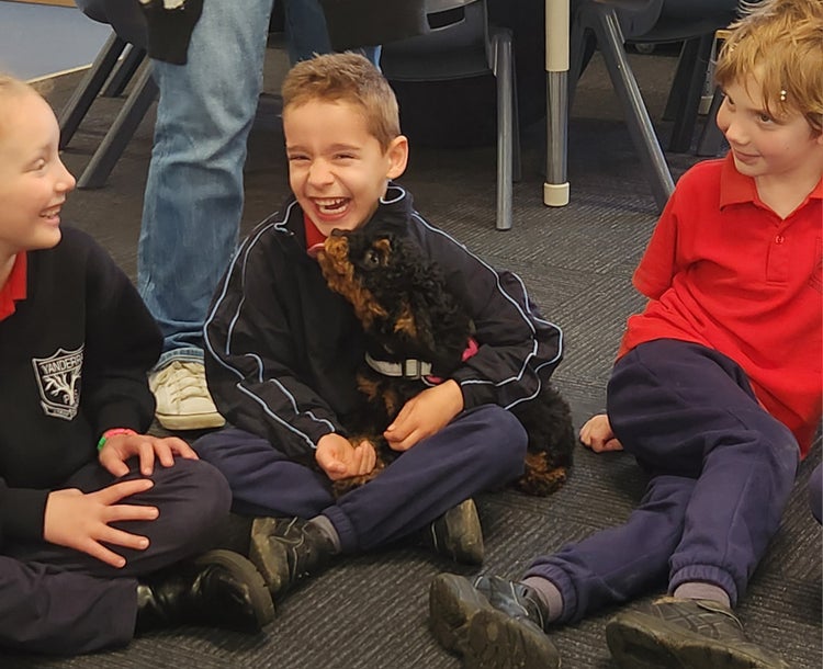 Three students sitting on the floor with a puppy