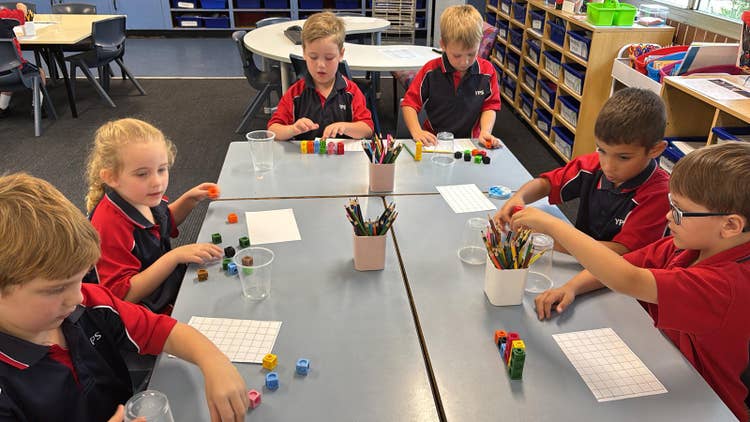 Six students sitting at desks doing maths with counters