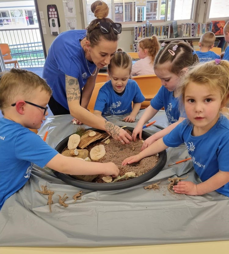 Photo of students playing in sand with an adult