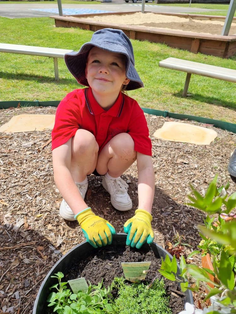 Student wearing gloves grouching in front of a garden bed